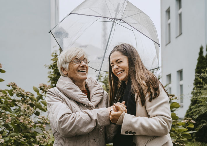 Photo of grandmother with granddaughter smiling and holding hands while under an umbrella in the rain