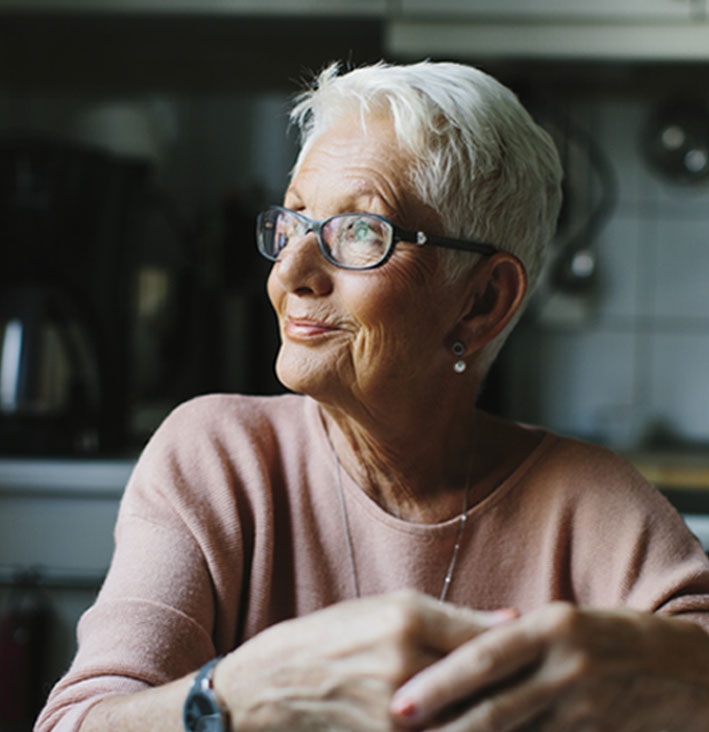 Photo of elderly woman looking into the distance and smiling while inside her home